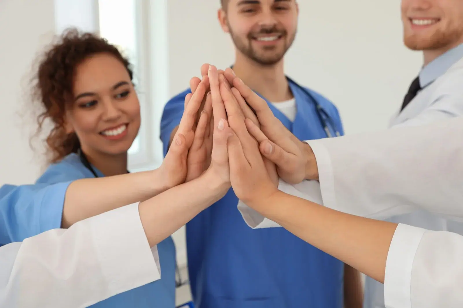 People in scrubs and white coats joining hands in a group high five.